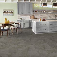 a large kitchen with grey cabinets and white counter tops is featured in this image, there are two chairs at the center of the table