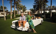 a man and woman sitting on the back of a white car in front of palm trees