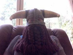 a person sitting in a chair with a knitted viking hat on top of their head