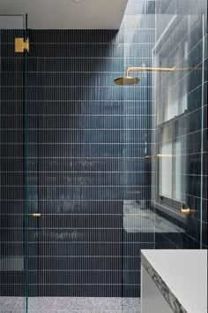 a bathroom with a glass shower door and black tiled walls, along with a white sink