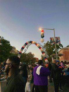 a crowd of people walking down a street next to an arch with decorations on it