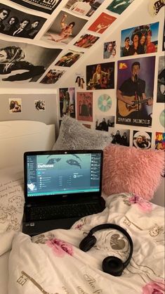 a laptop computer sitting on top of a bed covered in pictures and headphones next to a pink pillow