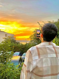 a man is taking a picture of the sunset with his cell phone while standing in front of some bushes