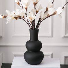 a black vase filled with white flowers on top of a table