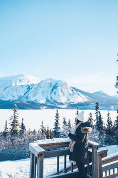 a woman standing on top of a snow covered slope next to a wooden fence and trees