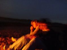 two people sitting next to each other in front of an open fire pit at night