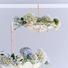 two vases filled with blue and white flowers hanging from wooden sticks in the air