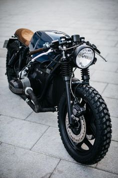 a black motorcycle parked on the side of a street next to a brick sidewalk with a wooden seat