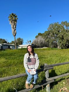 a woman sitting on a fence in the grass