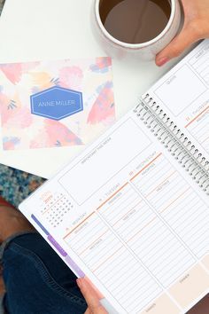 a person holding a planner next to a cup of coffee