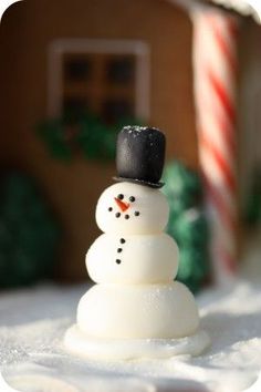 a snowman made out of marshmallows in front of a gingerbread house