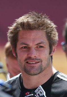 a close up of a person wearing a black shirt and smiling at the camera with other people in the background