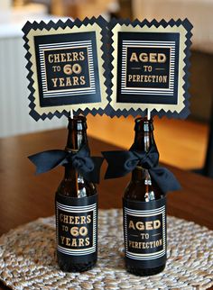 two beer bottles sitting on top of a table next to each other with signs that say cheers to 60 years