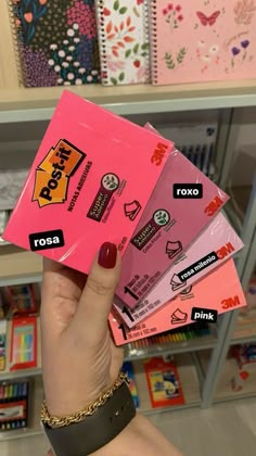 a person holding up five pink stickers in front of a book shelf filled with books