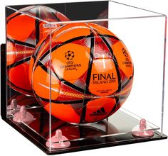 two orange soccer balls in a clear display case with gold bells on the bottom shelf