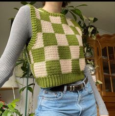 a woman is wearing a green and white knitted sweater over her shoulders, with a plant in the background