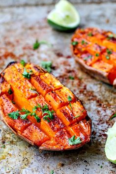 two grilled sweet potatoes on a baking sheet with limes and cilantro