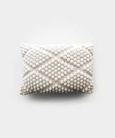 a white pillow with beading on the front and back, sitting on a gray surface