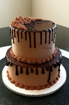 two tiered chocolate cake sitting on top of a white and black tablecloth covered plate