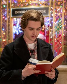 a young man reading a book in front of a christmas tree with lights on it