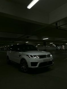 a white range rover parked in an empty parking garage with lights on above the car