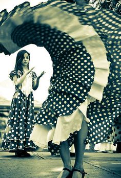 a woman in a polka dot dress is dancing on the street with an umbrella behind her