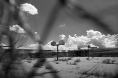 black and white photograph of street signs in the desert with clouds behind them on a sunny day