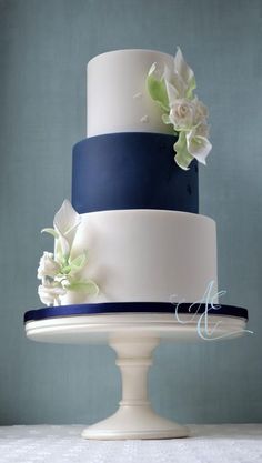 a three tiered cake with white and blue frosting on a pedestal in front of a wall