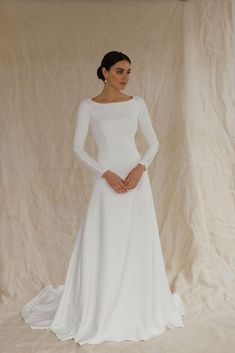 This unique wedding dress, made from luxurious crepe, is an ideal minimalistic elegance. With long sleeves and an A-line silhouette, this floor-length gown with a long train is perfect for winter weddings, including Christmas or civil ceremonies.  The modest design features a flattering boat neckline and a high back, creating a timeless and graceful look. Bridal buttons flow down the back and extend to the end of the train, adding a touch of classic beauty, long sleeves are also complemented wit A Line Long Sleeve Wedding Dress, Long Sleeve Wedding Dress Winter, Christmas Wedding Dress, Bridal Gown With Sleeves, Bridal Buttons, Winter Christmas Wedding, Wedding Dress Winter, Gown With Sleeves, Modest Wedding Dresses With Sleeves