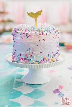 a birthday cake with sprinkles and a little mermaid tail on top is sitting on a table