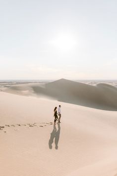 two people are walking in the sand dunes