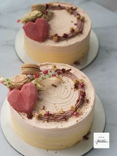 two cakes with frosting and hearts on top sitting on plates next to each other