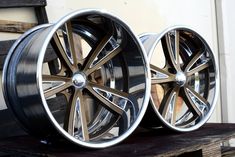 two black wheels are sitting on top of a wooden table and one is shiny silver