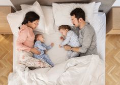 a man and woman are laying in bed with their two babys on the pillow