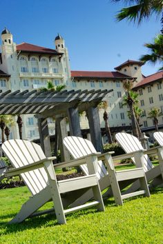 three white lawn chairs sitting in front of a large building with palm trees on the grass