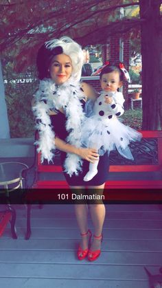 a woman holding a baby in her arms while standing next to a bench with a costume on