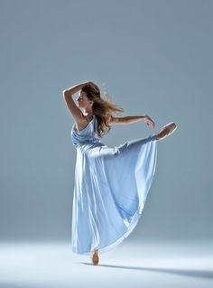 a woman in a blue dress is dancing with her arms behind her head and legs spread out