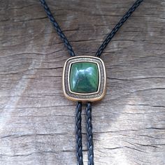 a necklace with a green stone and black braided leather cord on top of a piece of wood