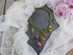 a necklace with flowers on it sitting on top of a piece of cloth next to a pink flower