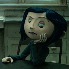 an animated doll sitting at a table with her hand on her chin and looking to the side