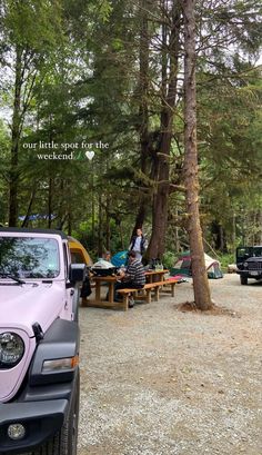 a pink jeep parked in front of a forest filled with trees and people sitting at picnic tables