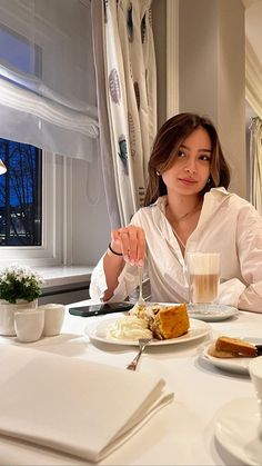 a woman sitting at a table with plates of food and drinks in front of her