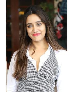 a woman with long brown hair wearing a white shirt and black and white checkered vest