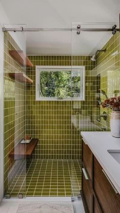 a green tiled bathroom with wooden cabinets and white counter tops, along with a window above the sink