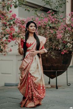 a woman in a red and white sari standing on the sidewalk with pink flowers behind her