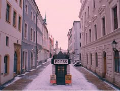 an empty street with snow on the ground and buildings lining both sides, in winter