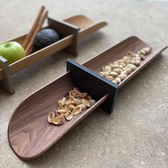 two wooden trays filled with nuts next to an apple and other items on the ground