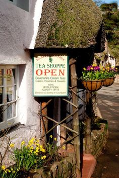 a sign that says tea shoppe open on the side of a building with flowers growing out of it