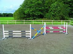 an empty horse paddock in the middle of a dirt field with trees behind it