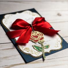 a close up of a card with a red ribbon on it and a rose in the middle